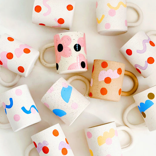 This handmade ceramic mug features playful polka dots over different shapes, adding a colorful and fun touch to your daily coffee or tea routine. Handcrafted with attention to detail, this unique mug is a must-have for any ceramic collection. Enjoy your favorite drink in a playful yet elegant way.