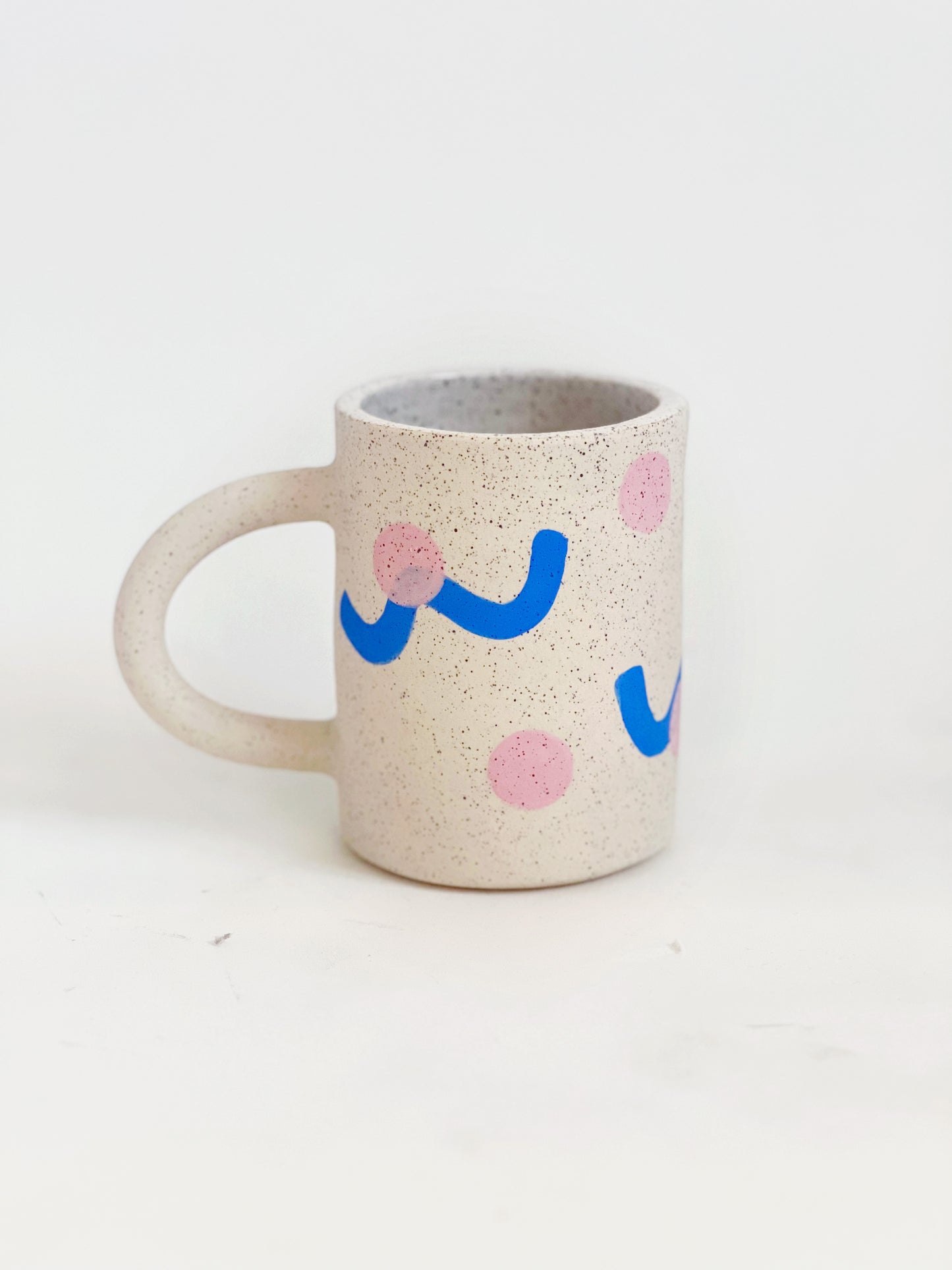 This handmade ceramic mug features playful polka dots over different shapes, adding a colorful and fun touch to your daily coffee or tea routine. Handcrafted with attention to detail, this unique mug is a must-have for any ceramic collection. Enjoy your favorite drink in a playful yet elegant way.