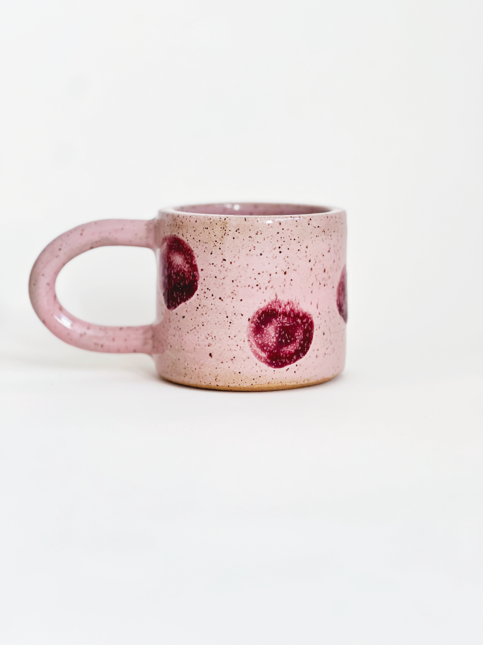 Pink speckled mug with red dots designs on a white background