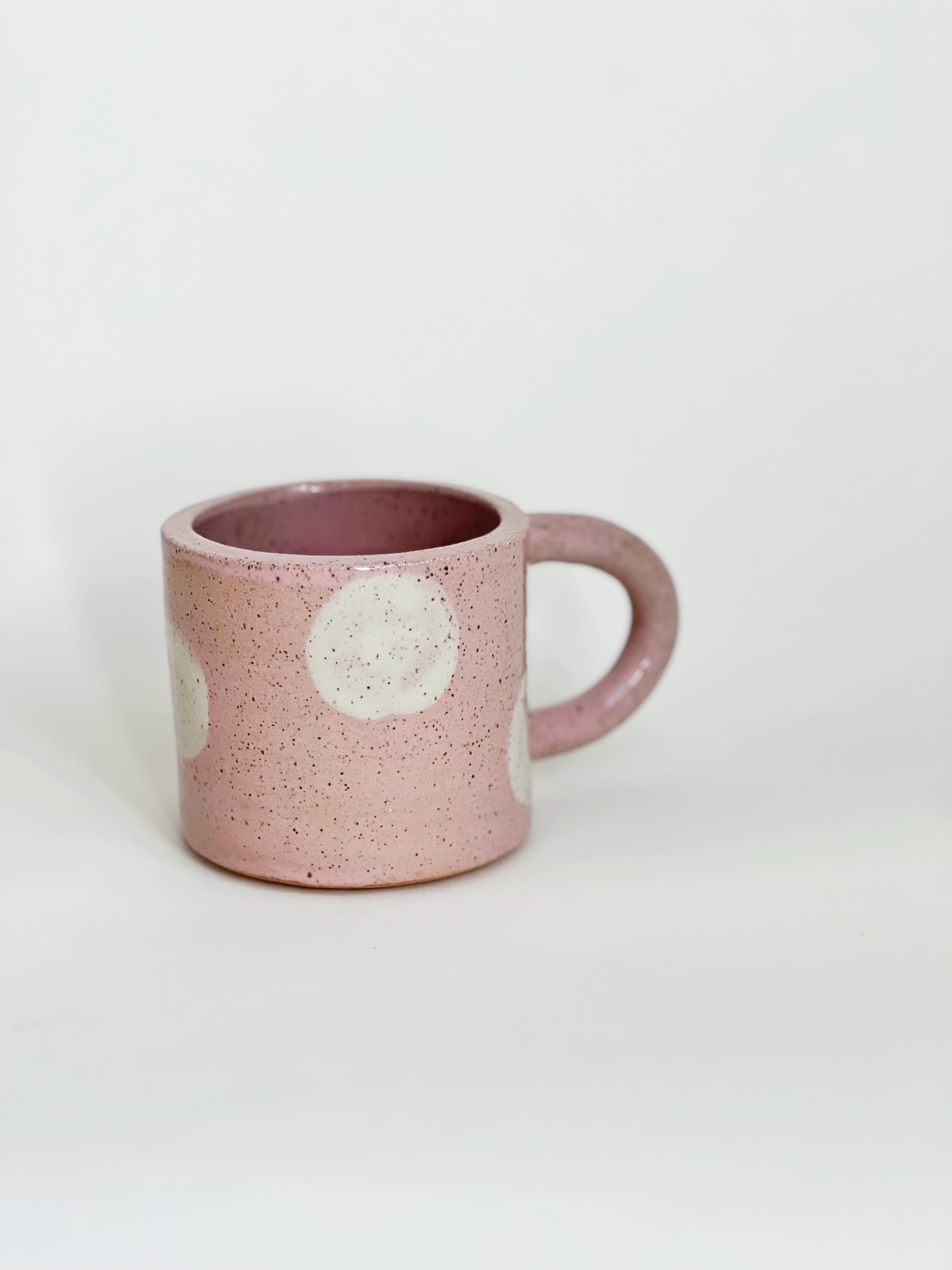Pink ceramic mug with white speckles and polka dots on a light gray background